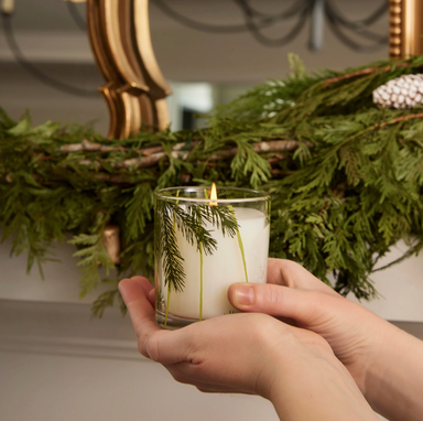 Frasier Fir Poured Candle, Pine Needle Design - Candle, clear vessel, with pine needles on the entire vessel, candle lit in front of a mantel